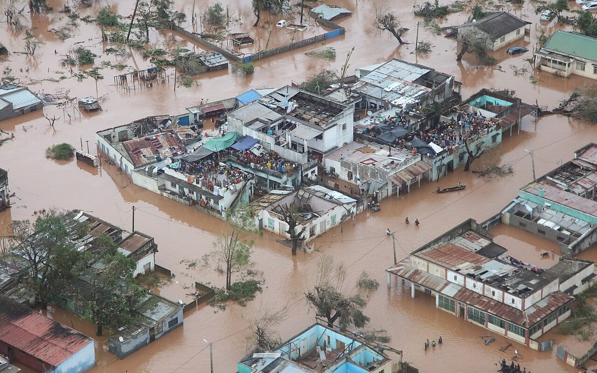 An aerial view of a town submerged by brown floodwater, with people on rooftops
