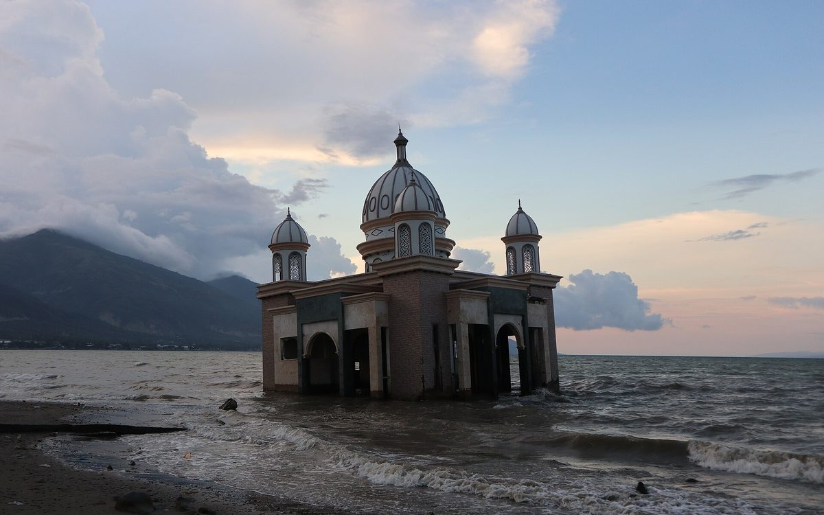 A domed mosque standing in the sea off the Palu coast, its supports collapsed, with mountains behind