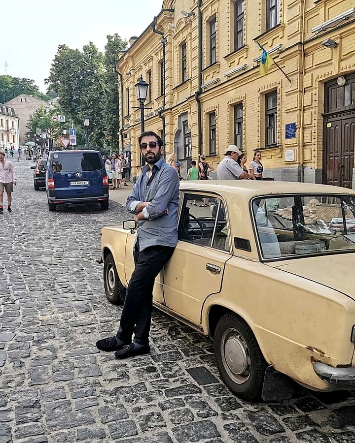 Kaiser Khan leaning on a vintage car on a cobbled street in Ukraine